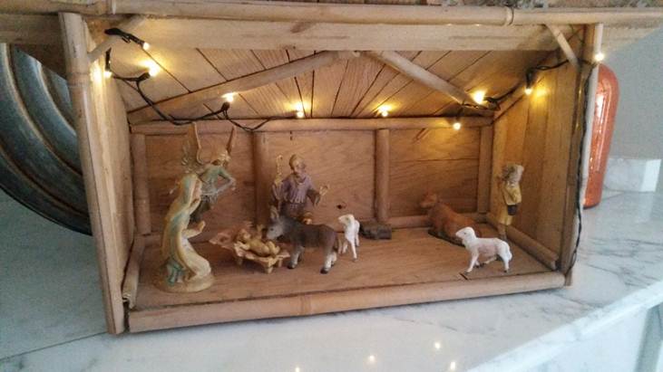 A table top Manger with Baby Jesus, Mary and Joseph, an Angel, a shepherd with a lamb on his shoulder, a cow, donkey and lamb looking at Jeus. 